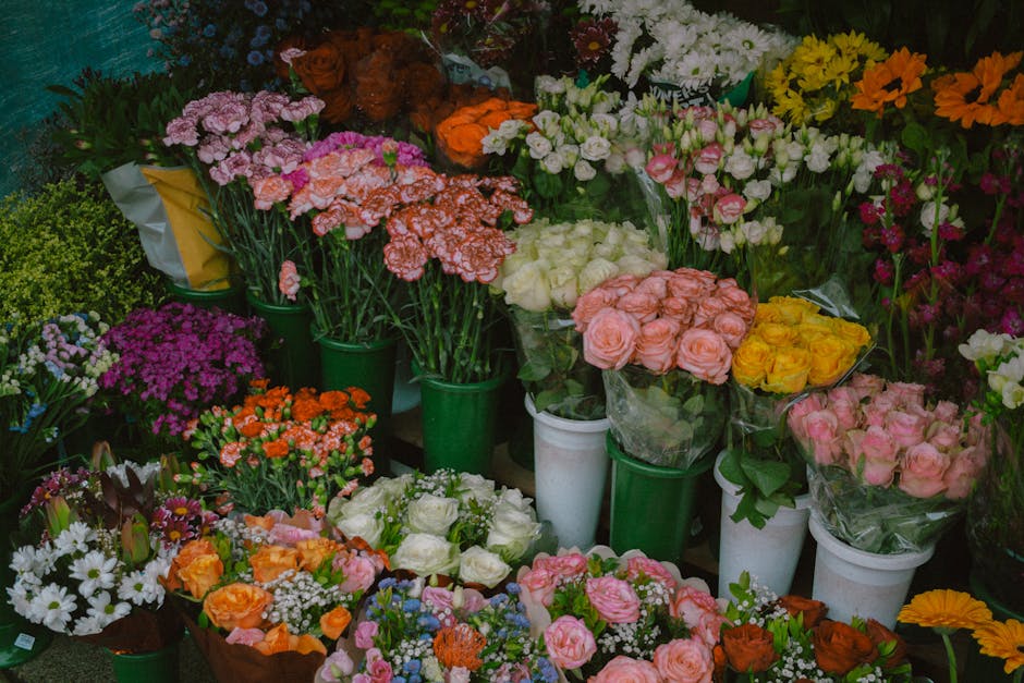 A vibrant display of fresh floral arrangements and bouquets at a flower shop, featuring a variety of flowers including pink roses, yellow roses, white roses, orange carnations, purple chrysanthemums, 