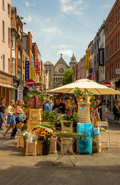 A vibrant outdoor flower market on St Mary Cray High Street BR5 featuring a variety of fresh flowers arranged in wooden crates and containers, including sunflowers, pink roses, and green foliage. The 